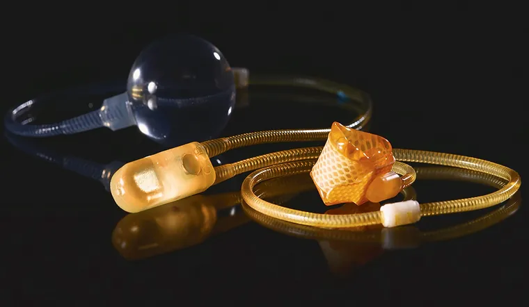 The three components of an artificial urinary sphincter photographed together: a clear pressure-regulating balloon, an amber control pump, and the woven cuff, joined by kink-resistant tubing.